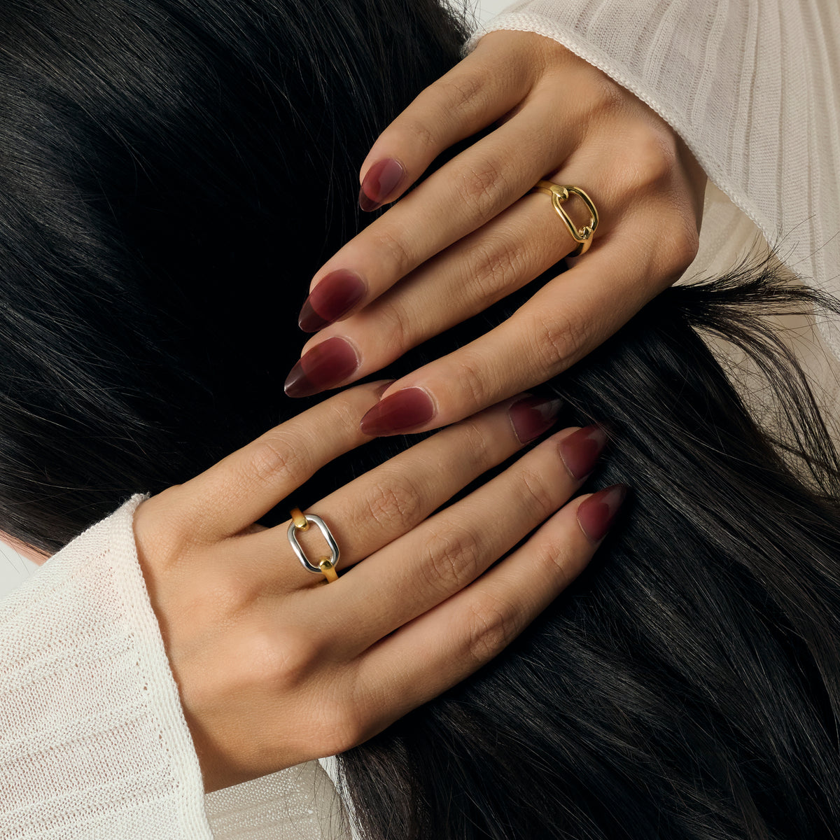 Close-up lifestyle shot of a woman's hands wearing a gold oval-motif ring and a two-tone gold and silver oval-motif ring, styled with a cream knit sweater. Nickel-free jewelry.

Photo lifestyle en gros plan des mains d'une femme portant une bague dorée à motif ovale et une bague bicolore dorée et argentée à motif ovale, agencées avec un tricot crème. Bijoux en acier inoxydable sans nickel.