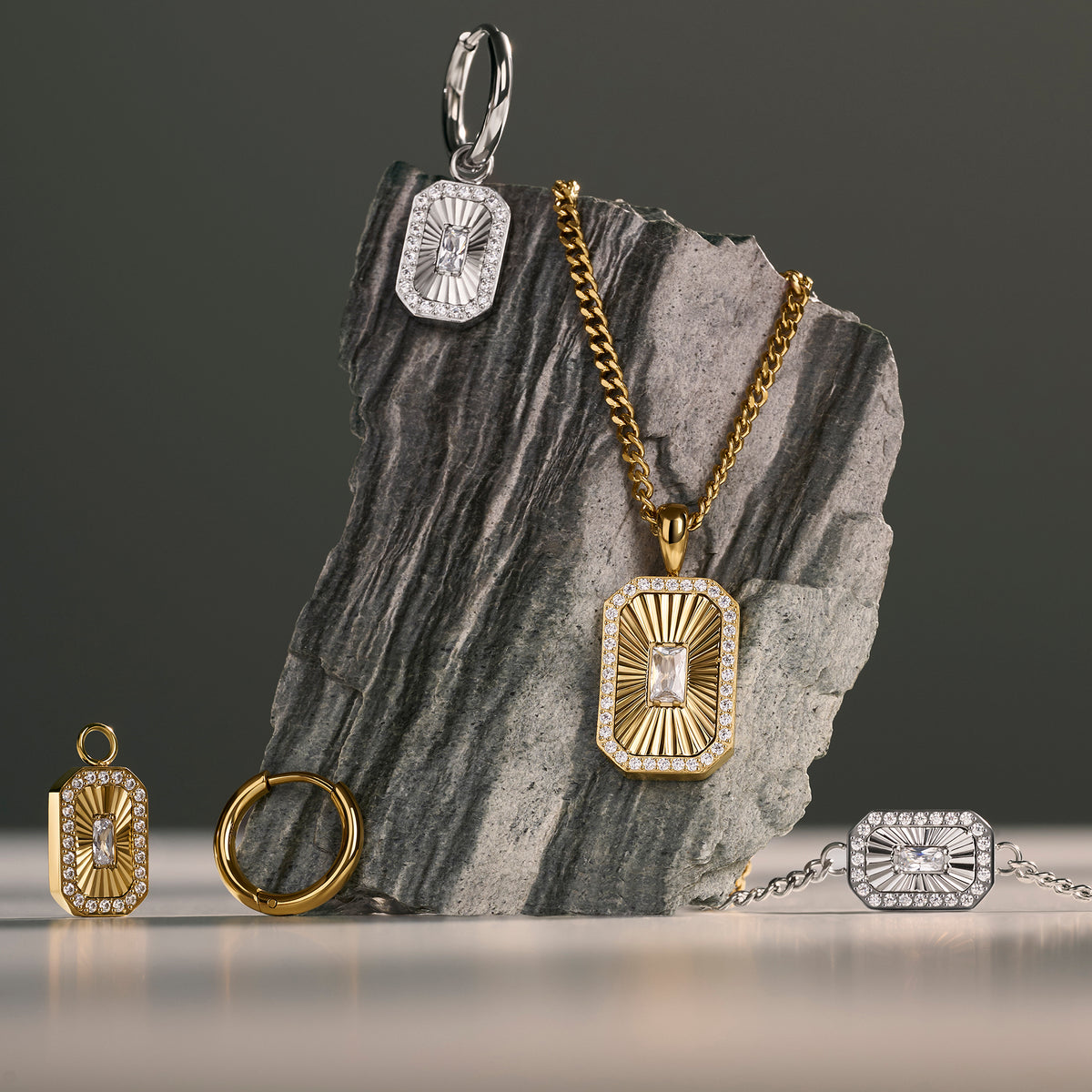 Gold and silver rectangular pendant jewelry with sunburst crystal detailing, displayed on a dark gray stone slab against a dark gray background. Jewelry by Mia Bijoux Canada.

Bijou à pendentif rectangulaire doré et argenté à motif rayonnant serti de cristaux, présenté sur une dalle de pierre gris foncé sur fond gris foncé. Bijoux par Mia Bijoux Canada.