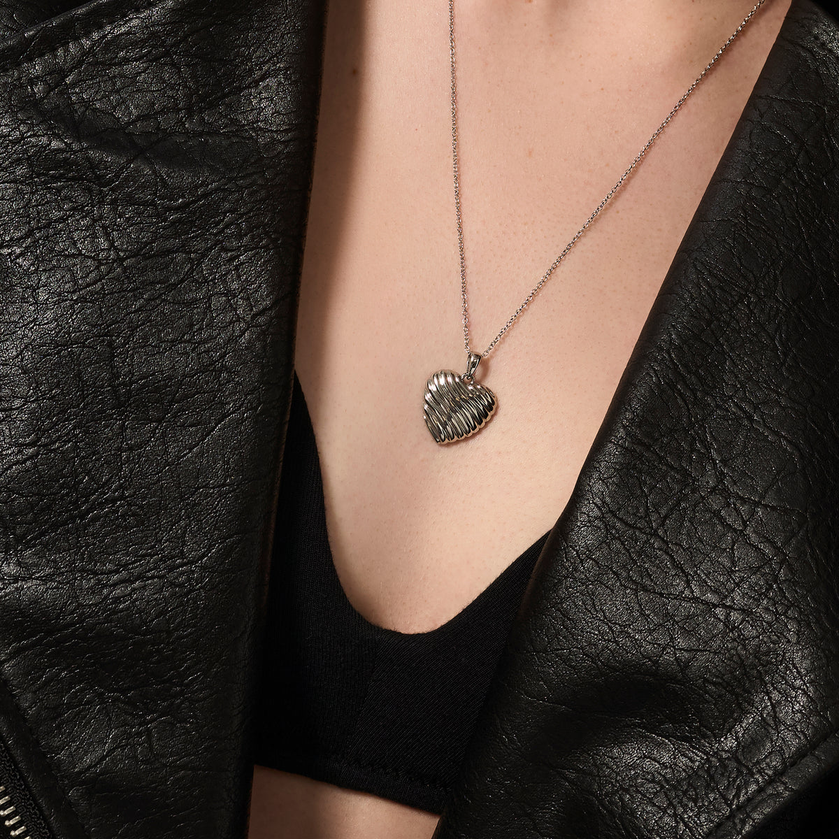 Silver stainless steel ribbed heart pendant necklace worn on neckline, sculptural romantic jewelry, hypoallergenic non-tarnish durable everyday necklace, modern elegant heart jewelry.
