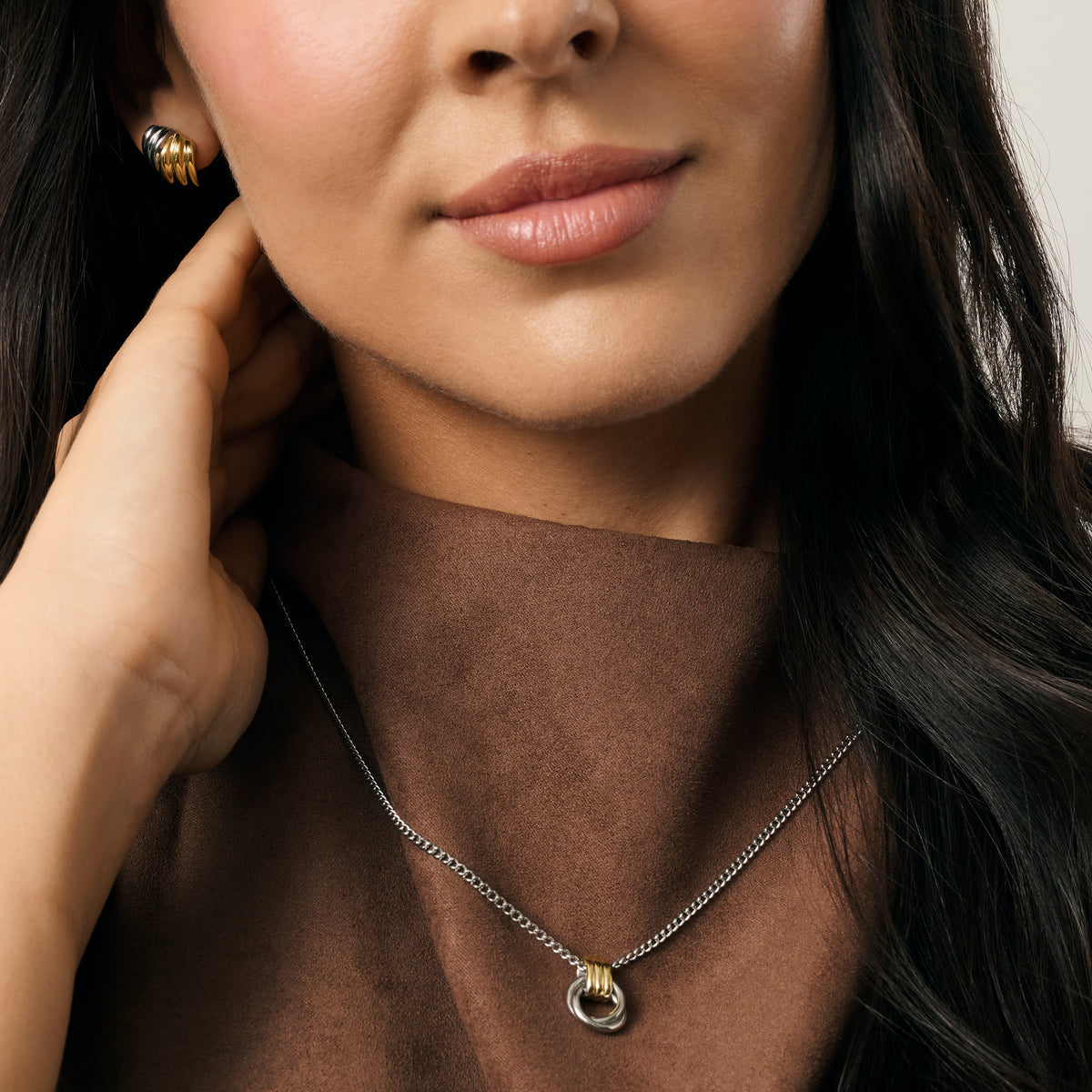 A close-up lifestyle shot of a model wearing a two-tone chain necklace and two-tone earrings paired with a brown top. Waterproof, stainless steel and allergy free. By MIAJWL.

Photo lifestyle en gros plan d'un mannequin portant un collier à chaîne deux tons et des boucles d'oreilles deux tons, agencés avec un haut brun. Résistant à l'eau, en acier inoxydable et hypoallergénique. Par MIAJWL.